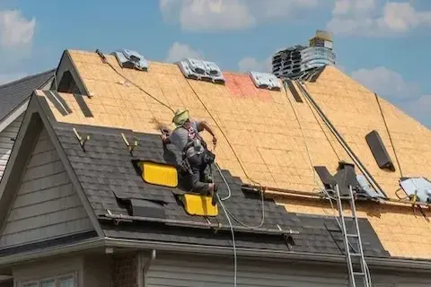 Roofer in safety harness removing old shingles during residential roof replacement