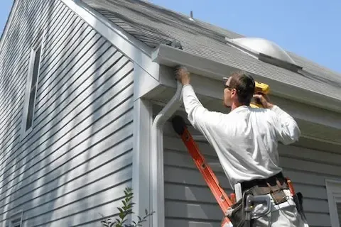 Technician on ladder fastening new gutter section to home fascia during gutter installation in Brooklyn Park