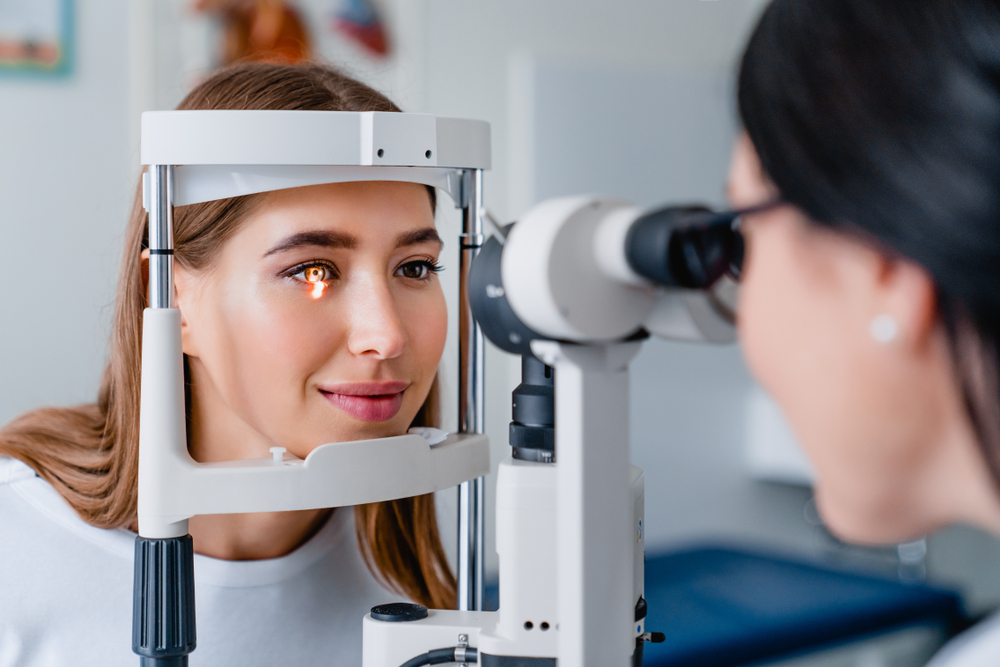Optometrist performing an eye exam for a seated patient using clinical equipment