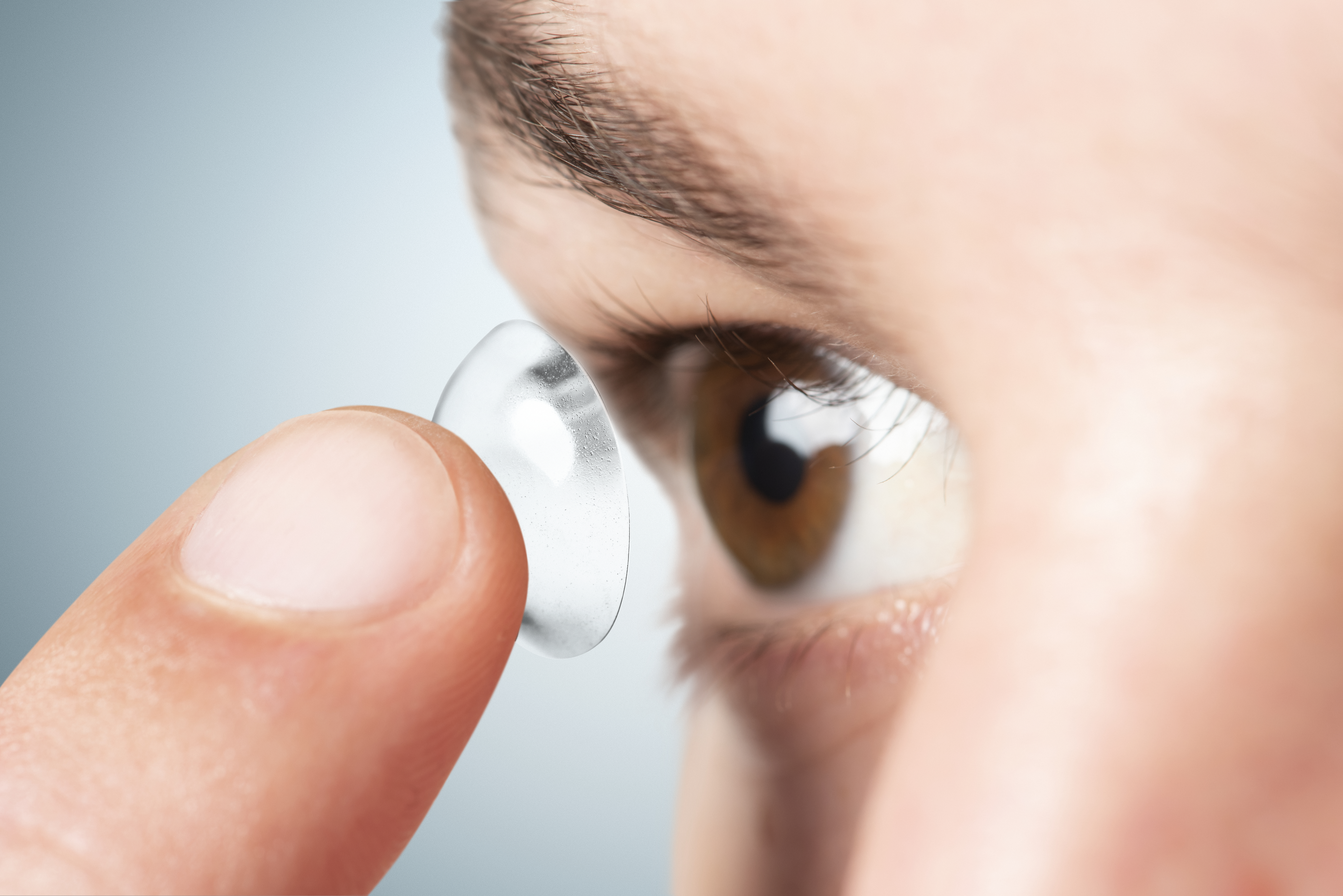 Woman applying a contact lens while looking in a mirror