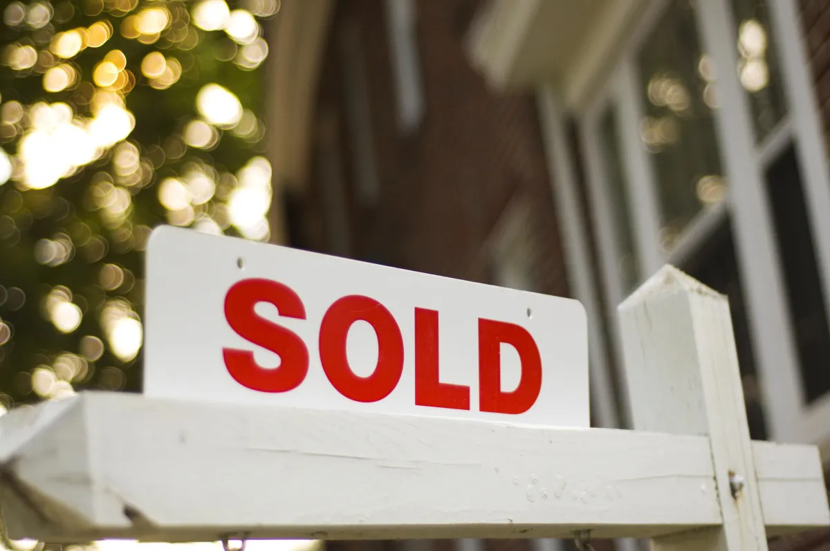 A white and red SOLD sign photographed in close-up, with warm sunlight blurred in the background.
