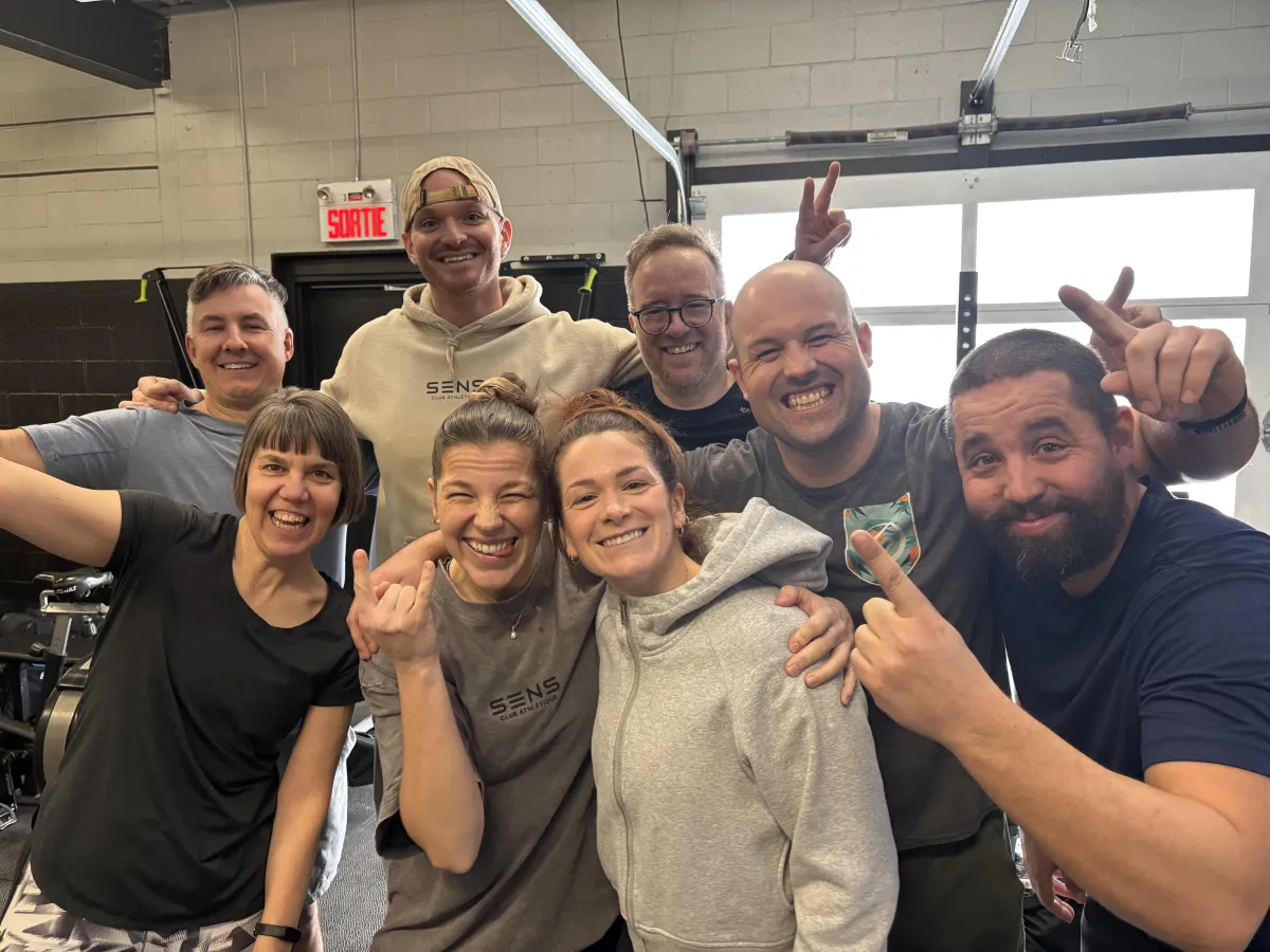 Groupe de membres s’entraînant dans un petit gym, coach encourageant, ambiance chaleureuse et motivante, illustrant la puissance de la communauté et la constance.