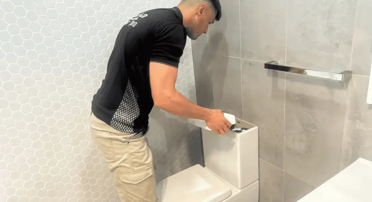 Plumber repairing a leaking pipe under a kitchen sink in Western Sydney