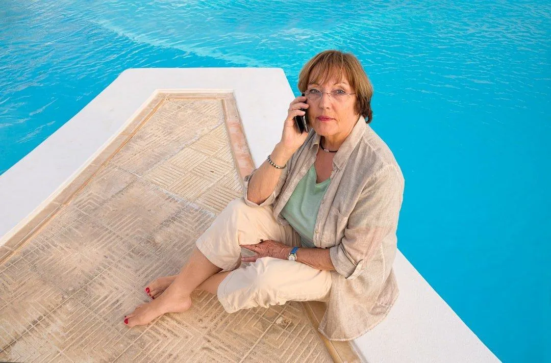 A woman relaxes comfortably by the pool, enjoying the sunny day in a casual, laid-back pose.