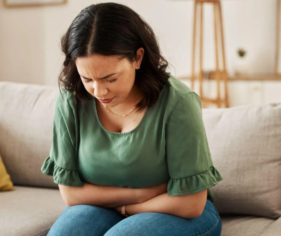 A woman holds her stomach with a pained expression, clearly experiencing belly discomfort.