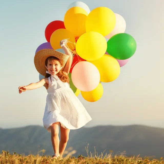 Girl running with balloons in a field looking confident