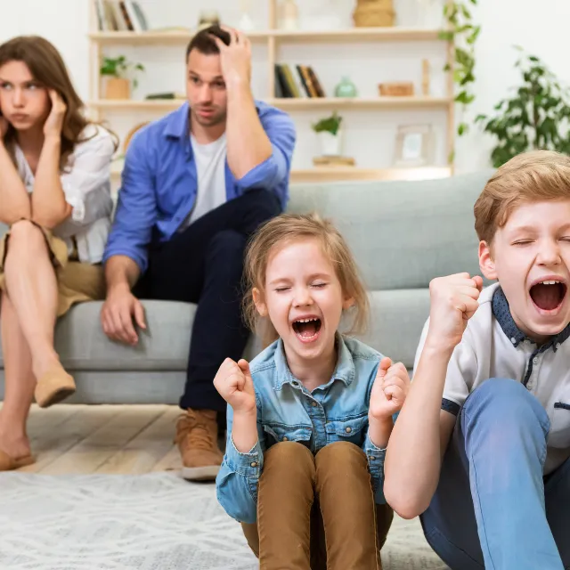 parents sitting on a sofa looking overwhelmed while children shout showing big emotions