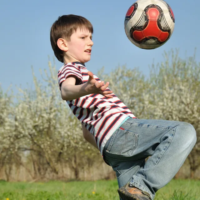 Boy kicking a football outdoors, using physical activity and movement as a healthy way to manage emotions and reduce stress.