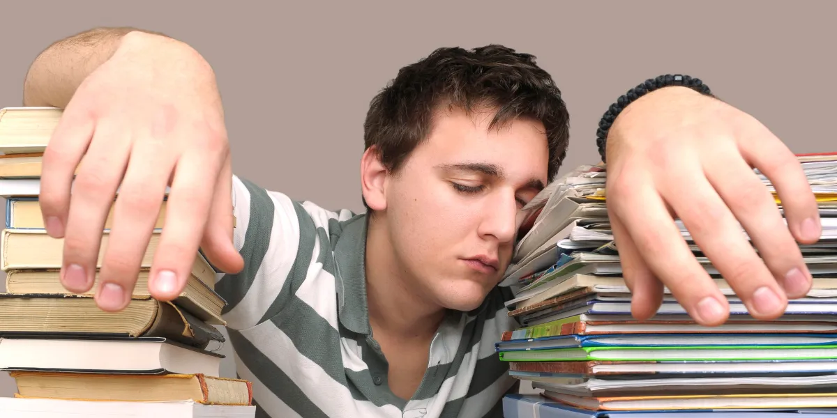 Teenage boy asleep between two stacks of books, illustrating the importance of sleep and rest for learning, concentration and emotional wellbeing.