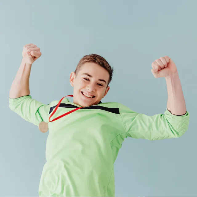Teenage boy standing proudly with his arms raised and a medal around his neck, representing confidence, achievement, self-belief and personal success.