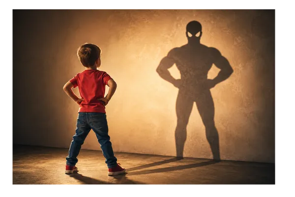 Young child standing confidently while the shadow of a superhero stretches in front of him, symbolising the courage children often find in imagination during difficult times.
