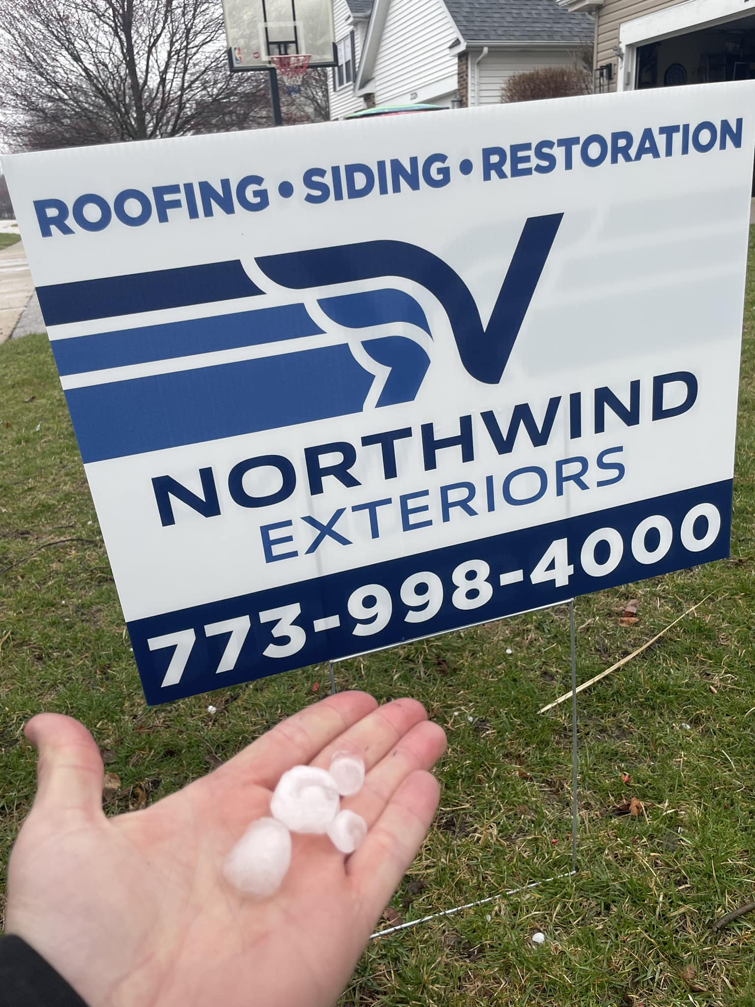 Large hail held in hand next to a Northwind Exteriors yard sign after the March 10, 2026 storm in Chicagoland, offering free roof and siding inspections.