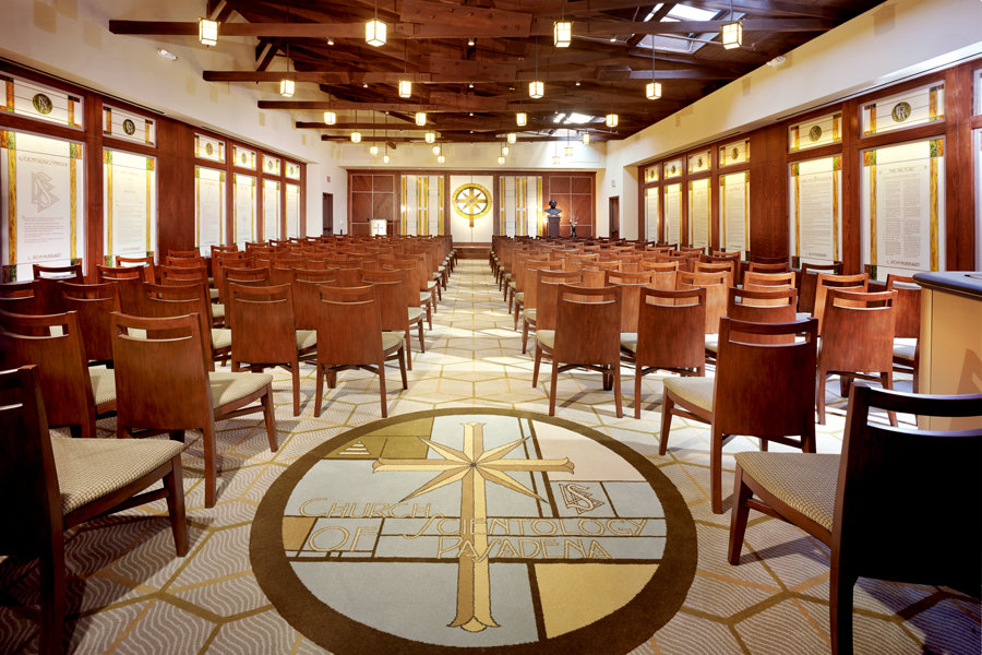 A respectful image of a sunlit chapel interior, rows of wooden pews adorned with white flowers, and soft natural light streaming through stained glass windows. The setting is serene and welcoming, evoking a sense of peace and community gathering for a meaningful memorial service.
