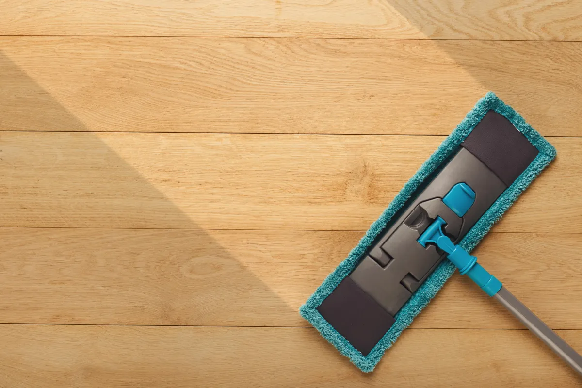 Close-up of a broom sweeping a tiled floor, with visible dust and debris being collected, emphasizing cleanliness and floor maintenance.