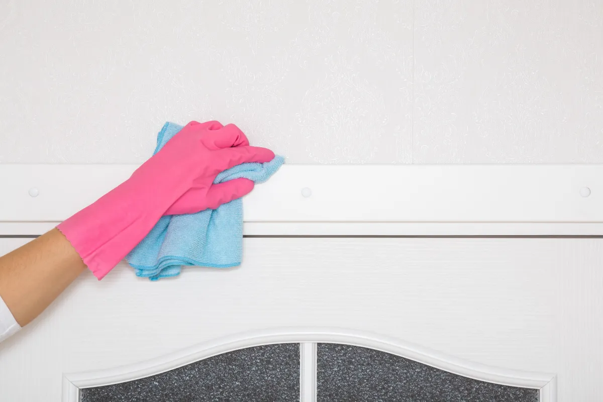 Close-up of a gloved hand cleaning a white baseboard with a cloth, removing dust and dirt, highlighting detailed cleaning and home maintenance.