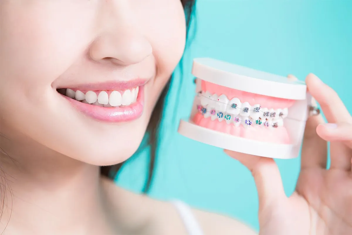 Patient smiling while holding a dental model with braces at Kong Dental Surgery in Singapore.