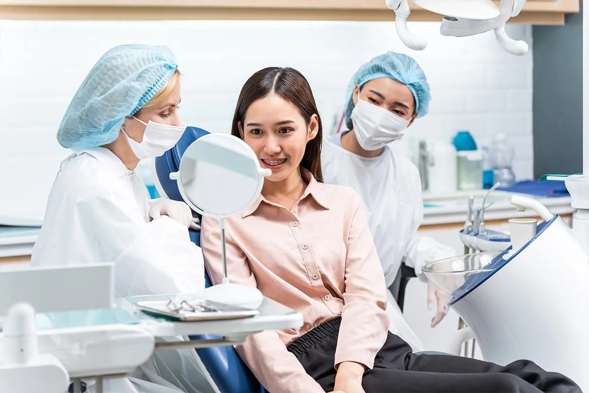 Patient smiling in the mirror after braces treatment at Kong Dental Surgery in Singapore.