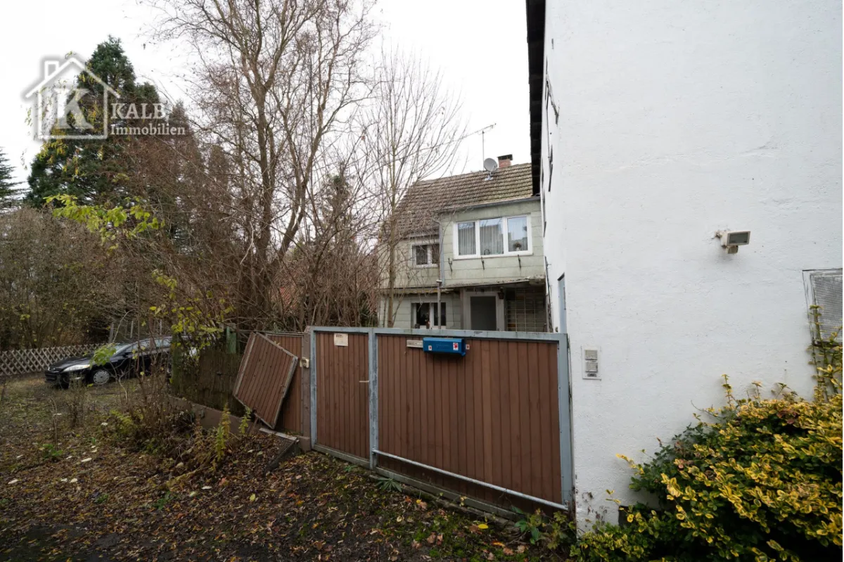 Zugang zum Grundstück mit Holz- und Metalltor, umgeben von Bäumen und Sträuchern. Außenbereich in naturbelassenem Zustand mit Renovierungsbed
