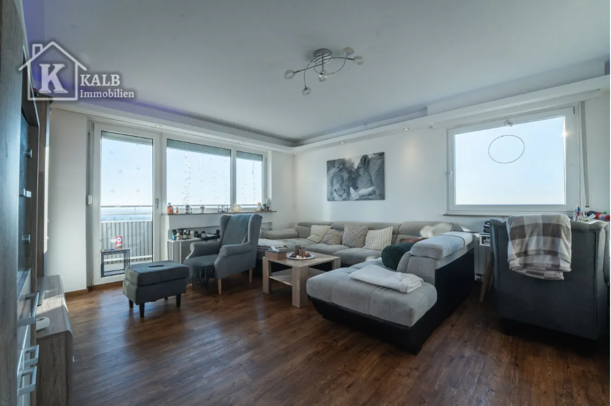 Helles und großzügiges Wohnzimmer mit moderner Eckcouch, großen Fensterfronten und Zugang zum Balkon; beeindruckender Weitblic