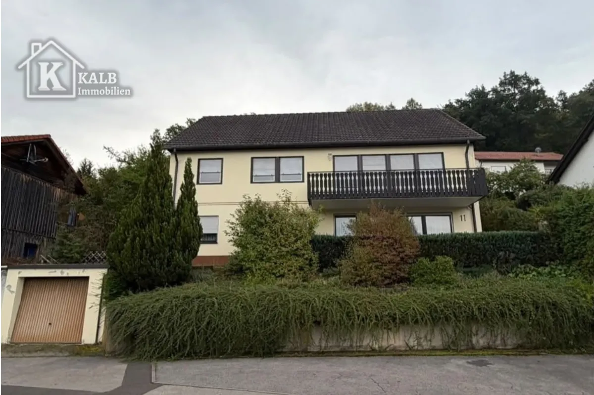 Außenansicht des Wohnhauses mit Balkon, Gartenbepflanzung und Garage