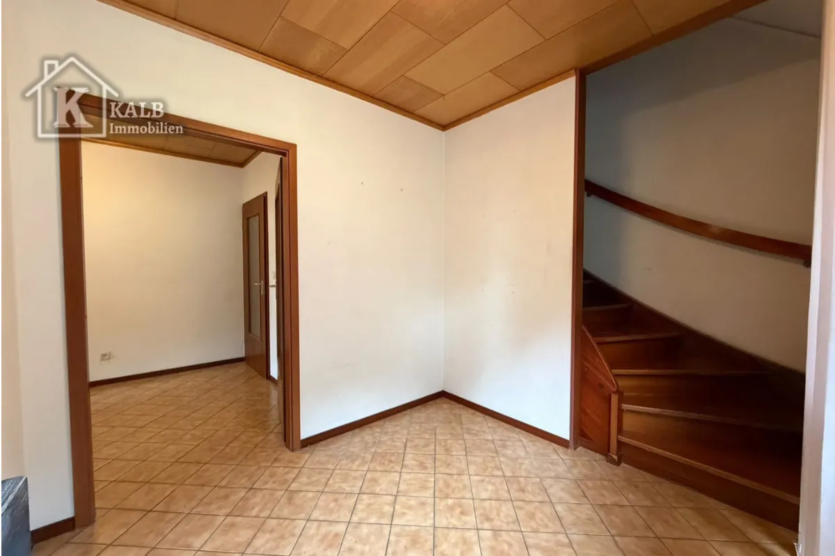 Gefliester Eingangsbereich mit Holztreppe und Durchgang zu weiteren Räumen