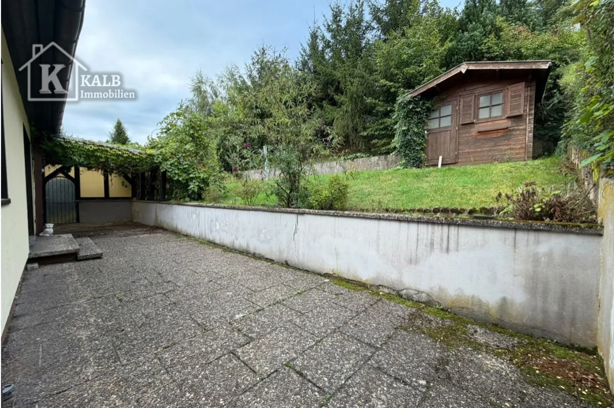 Gepflasterter Außenbereich mit angrenzender Grünfläche und Gartenhaus
