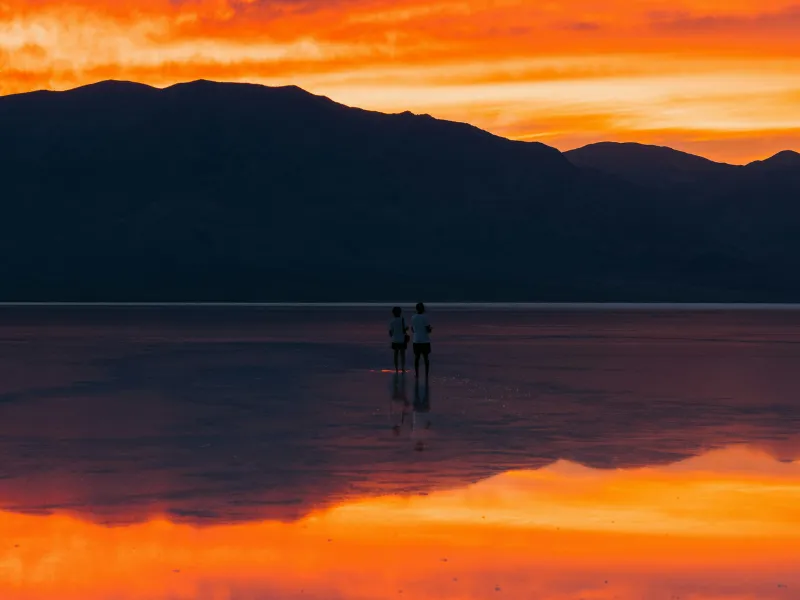 a vibrant sunset over a calm, reflective surface, likely representing Badwater Basin in Death Valley National Park, California