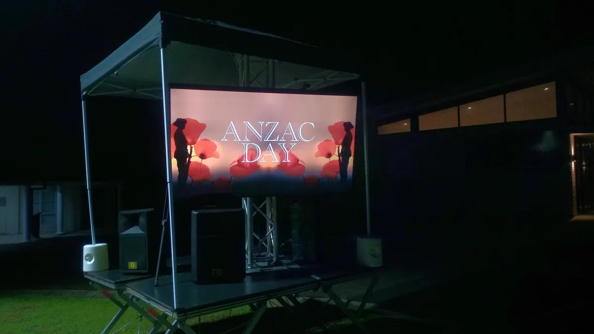 High-brightness 75 inch LED screen on truss mount with outdoor PA speakers on a mobile stage under a gazebo canopy