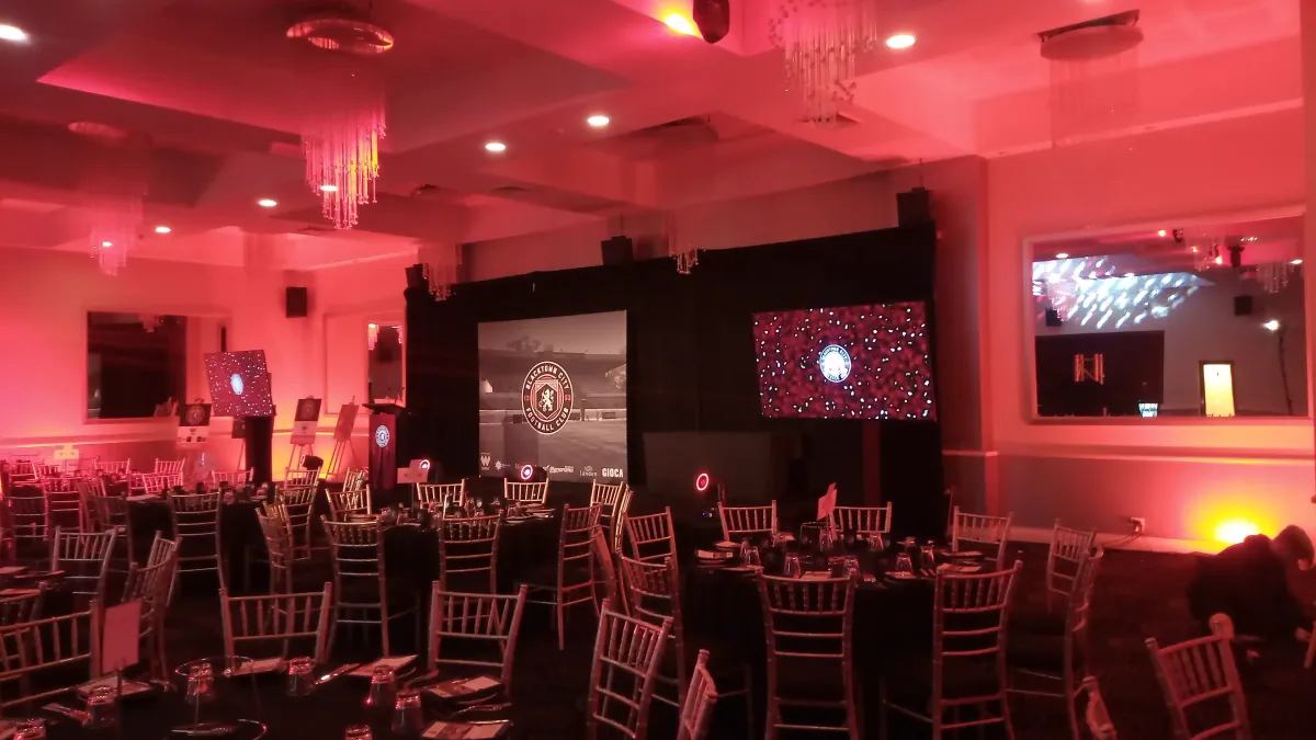 Large LED screens with red ambient stage wash lighting and professional PA speakers for a corporate football club gala