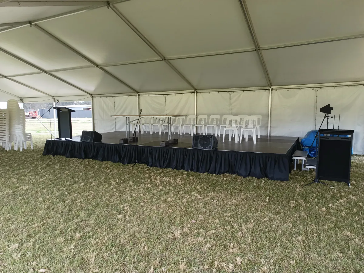 Professional outdoor stage setup with black skirting, wedge floor monitors, and a lectern under a white marquee tent.