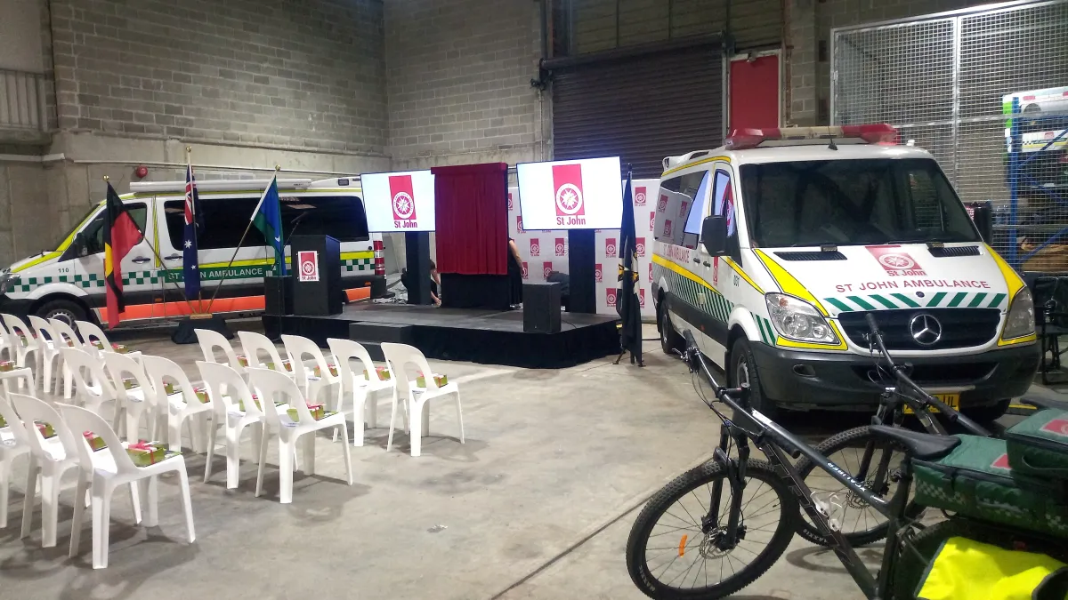 Dual 75 inch LED monitors on heavy-duty stage stands with a professional lectern and PA system in a warehouse venue.