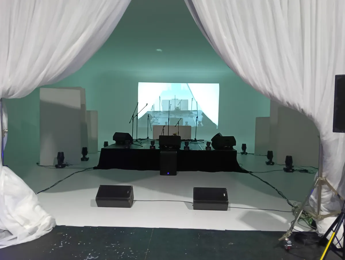 Professional stage setup with active floor monitors, DMX LED wash lighting, and a white drape backdrop for live performance
