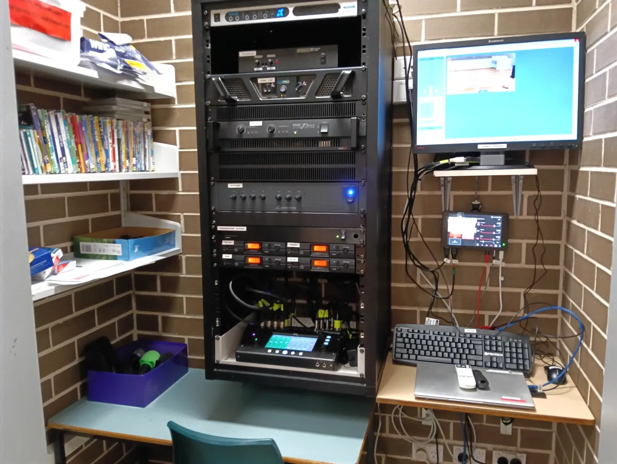 Professional 19-inch equipment rack with digital audio processors, power amplifiers, and a touch-screen control interface