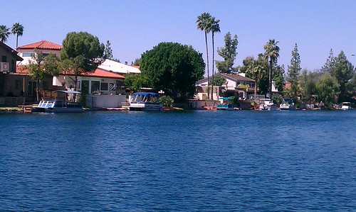 A close-up of hands in a meditative mudra, resting on crossed legs, with soft sunlight filtering through. The background is a tranquil indoor yoga space with natural textures and calming colors, evoking peace and mindfulness.