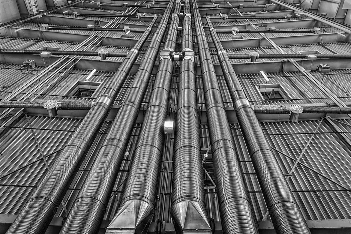 Large industrial plumbing and ventilation pipes installed in a commercial building interior, showing complex piping infrastructure.
