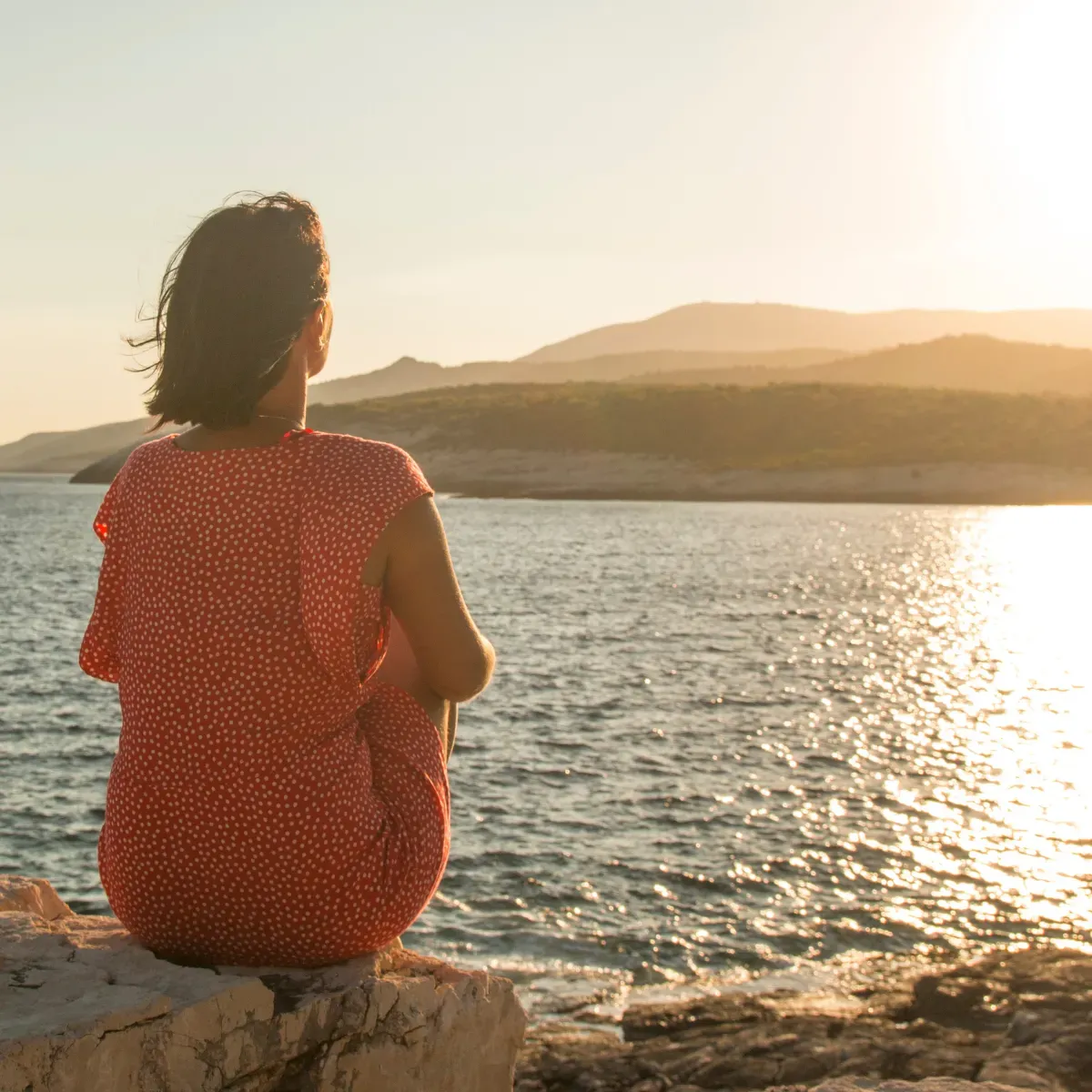Woman sitting on rock looking at water