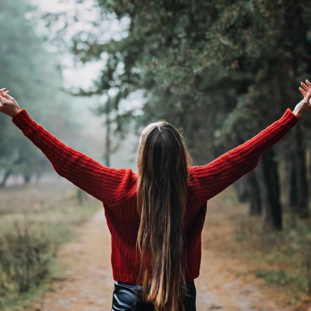 Person standing outside with arms up, and while looking up towards the sky.