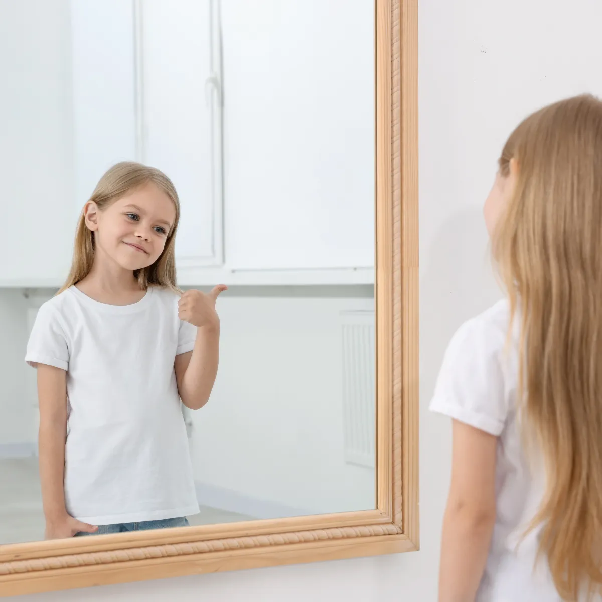 Young girl looking in the mirror and giving herself a thumbs-up.