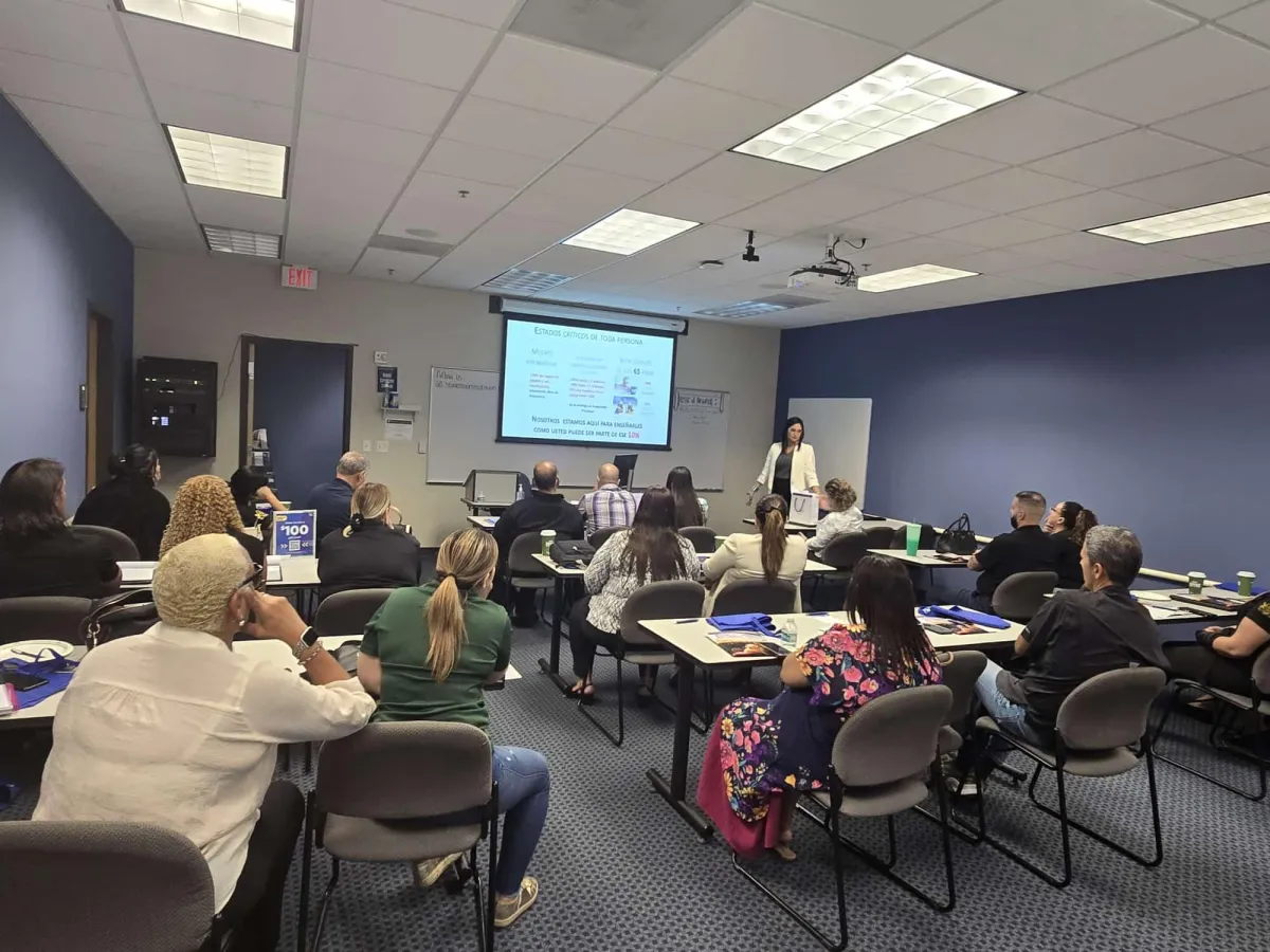 A smiling Hispanic couple sits together at a kitchen table, reviewing financial documents and a tablet. The kitchen is bright and modern, with blue and white decor. Their expressions show relief and optimism, highlighting the positive impact of financial guidance.