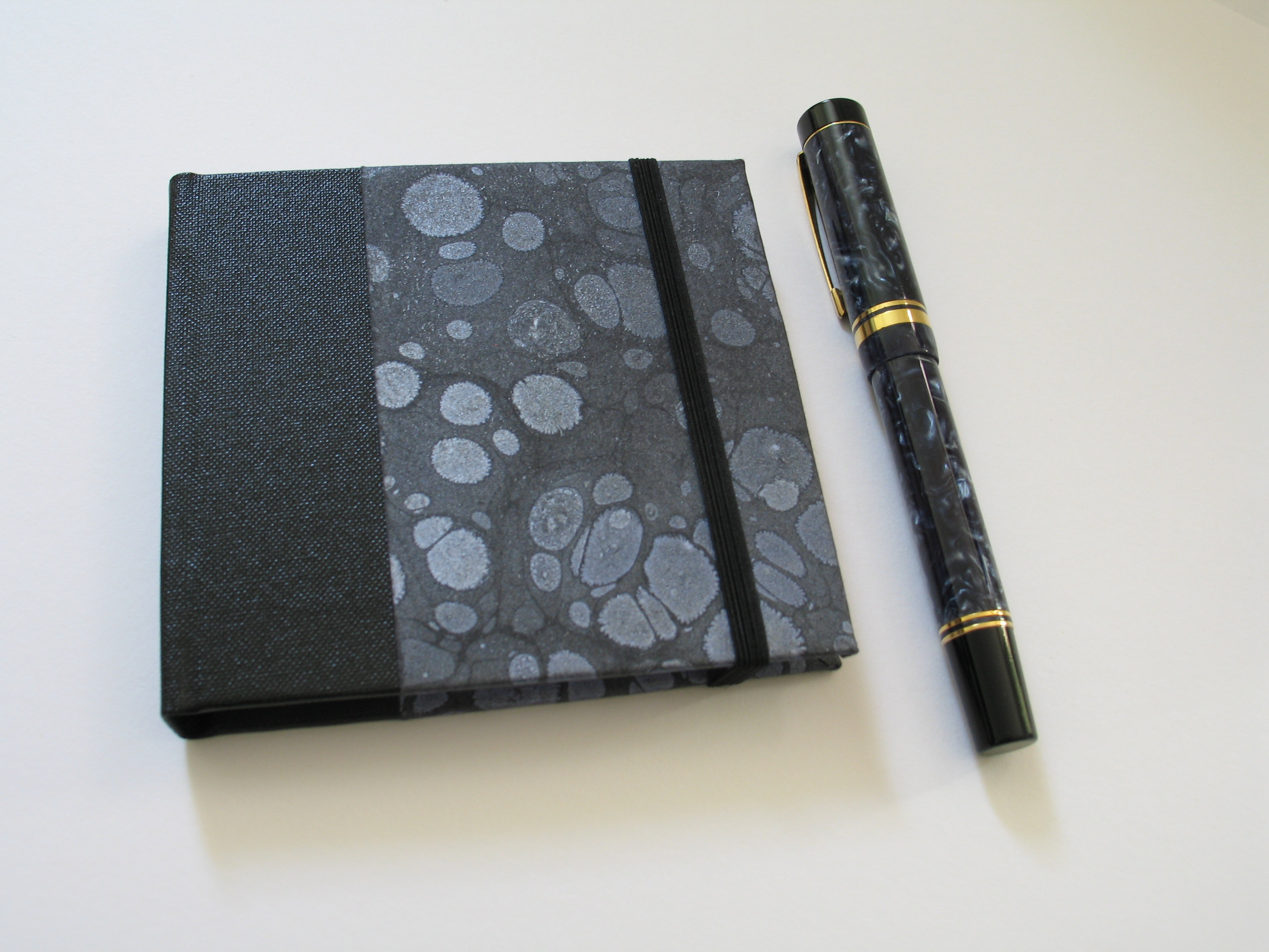 A pastel-hued, hand-bound journal with visible stitching, resting on a linen cloth beside a vintage fountain pen and dried lavender, softly lit in a sunlit studio. The image evokes warmth, craftsmanship, and a sense of calm.