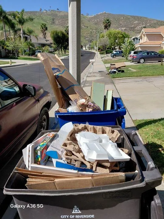 A blue recycling bin filled with discarded cardboard, household waste, and construction materials during junk removal by Rabbits Services in Riverside.