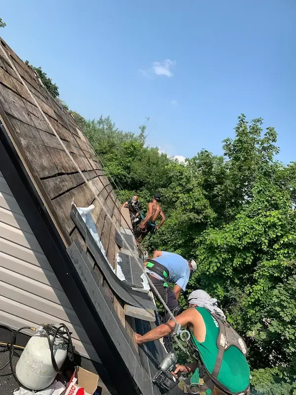 A team of professional A-OK Roofing contractors performing comprehensive roof maintenance and structural inspection on a steep-slope residential roof in Toronto. Fully harnessed roofers are seen utilizing pneumatic tools and safety equipment to repair wood decking and secure roofing materials. Highlights expert preventative maintenance designed to extend roof lifespan for homeowners across East York and the Greater Toronto Area.