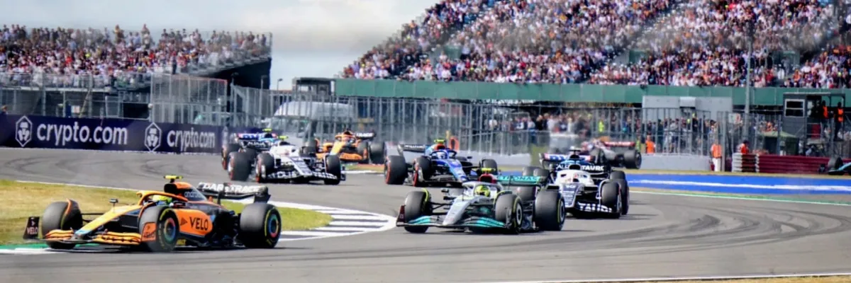 Luxury coach arriving at a famous European racetrack with excited motorsport fans and grandstands in the background