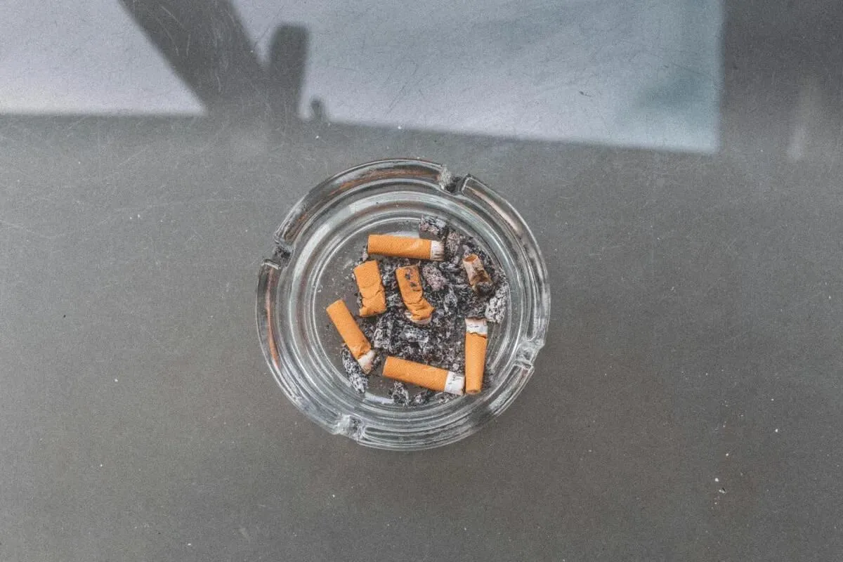 A glass ashtray filled with cigarettes placed on a flat surface, surrounded by an indoor setting with orange tones.
