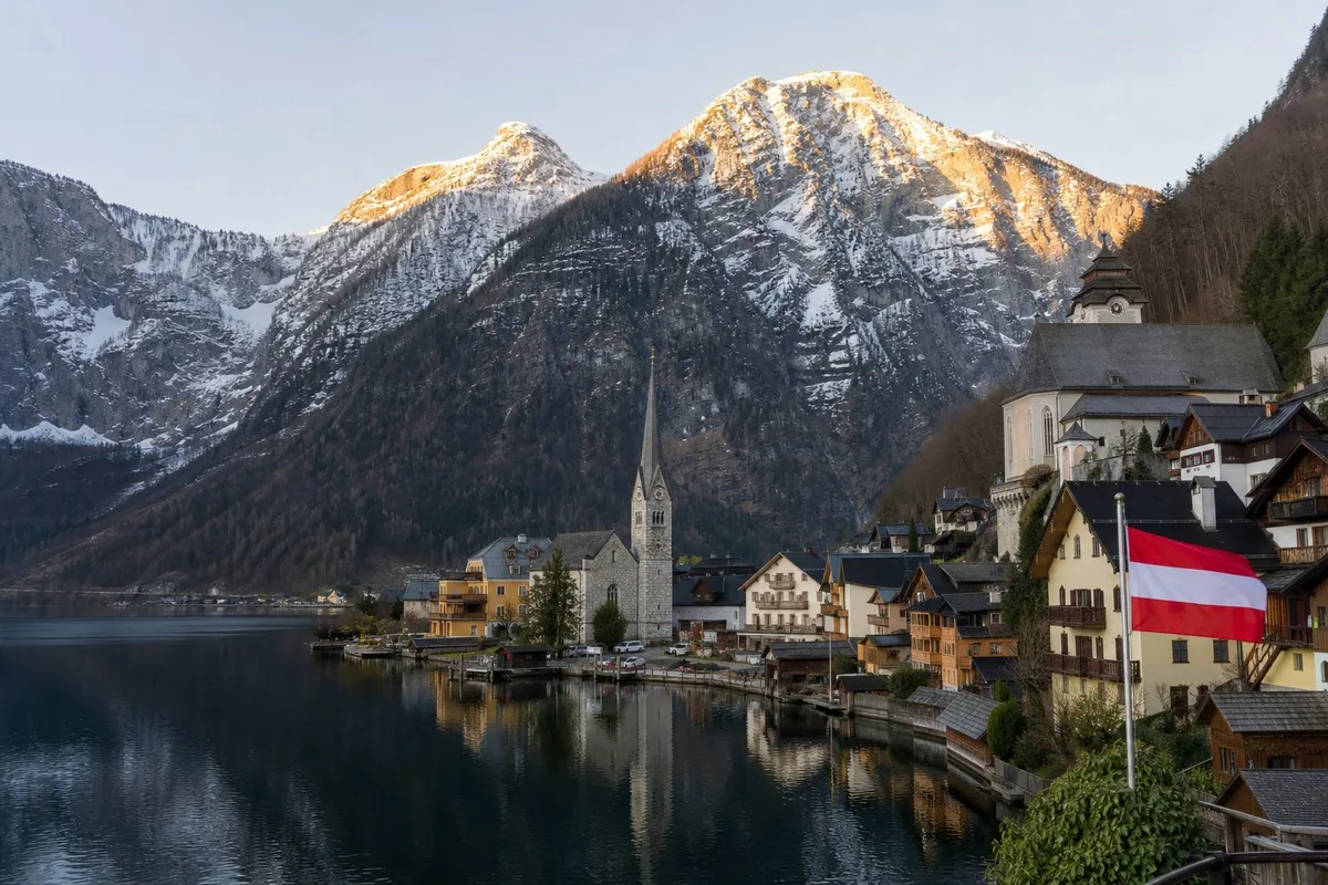 Snow-dusted alpine village rooftops and church spire below forested slopes in cold morning light