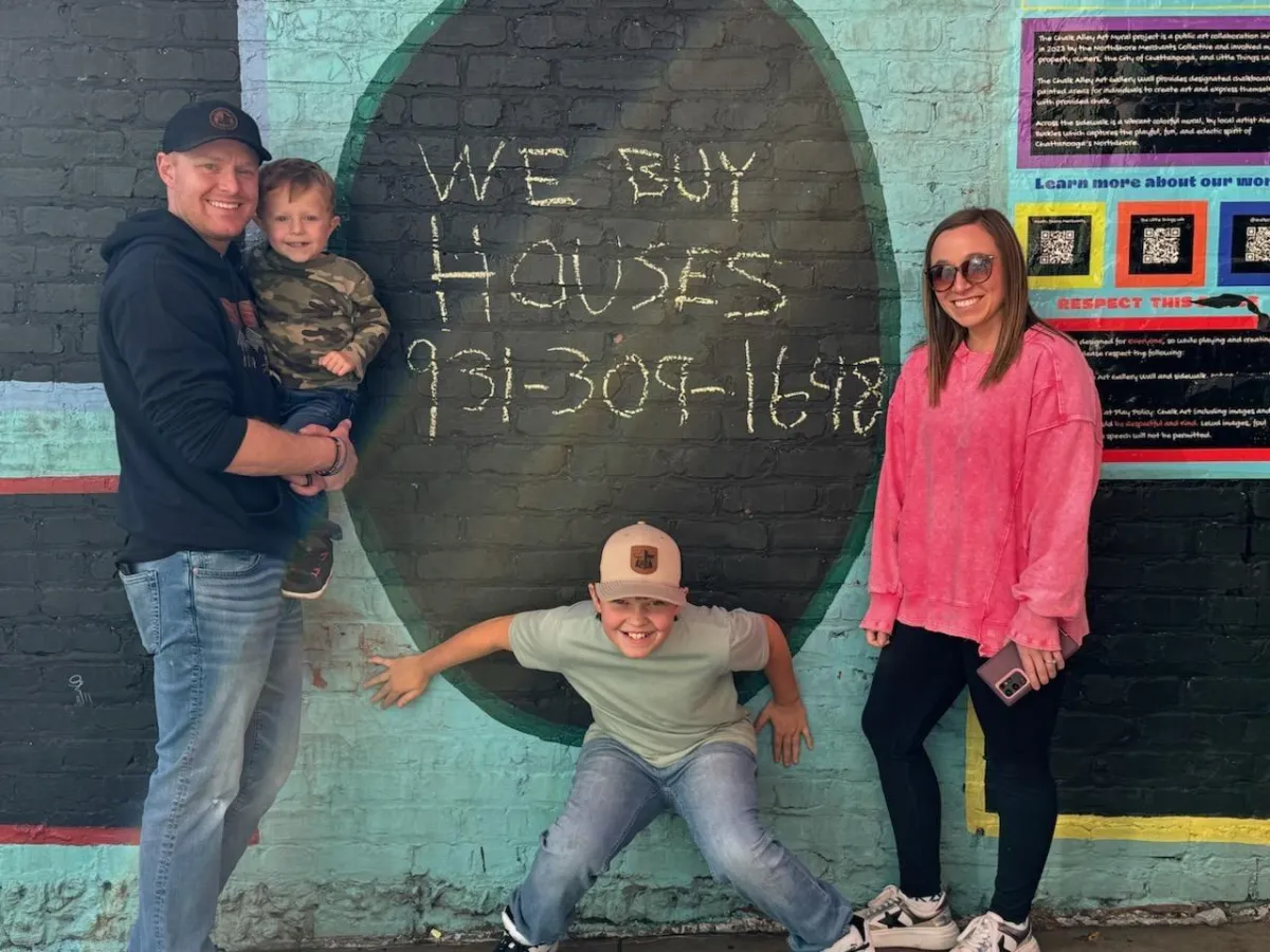 family of four, two adults, two children standing in front of a colorful brick wall with a phone number written in chalk