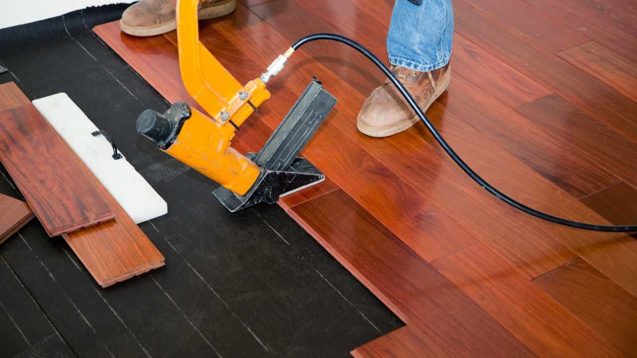 A man is engaged in installing wood flooring with a power tool.