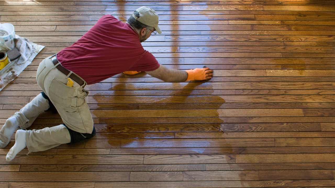 A man is kneeling on the floor painting a wooden floor.