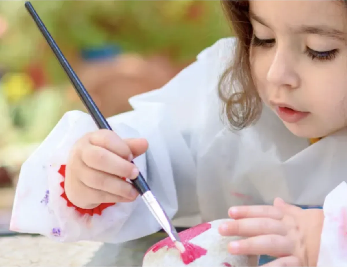 Girl paints a rock with a paintbrush