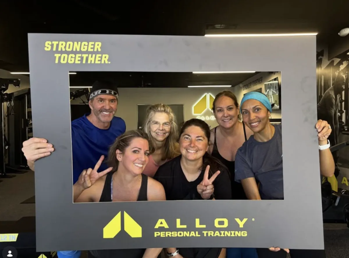 A group of clients smiling and posing in a photo frame after a small group personal training session at Alloy Personal Training, showcasing the community atmosphere and support during their fitness journey.